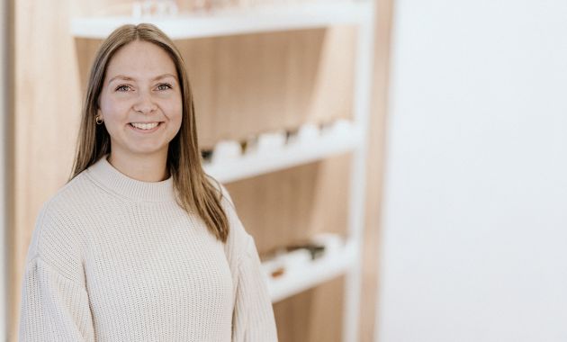 Julia Storck steht lächelnd in einem hellen Fachgeschäft vor einer Präsentationswand.