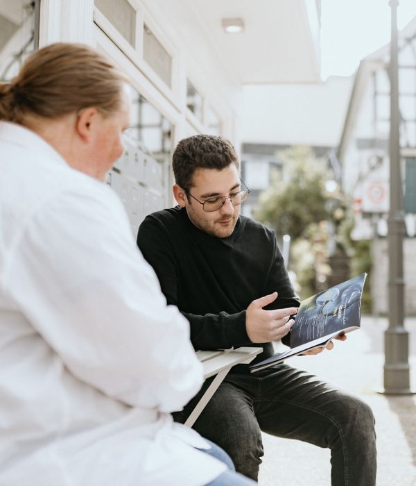 Joshua Jäger und Mark Gundlack sitzen draußen im Beratungsgespräch und schauen gemeinsam in eine Broschüre.
