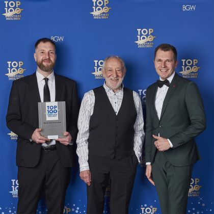 Michael Männing und Lars Rudloff stehen mit Dieter Hallervorden vor einer TOP 100 Akustiker-Fotowand; Lars Rudloff hält die Auszeichnung in den Händen.